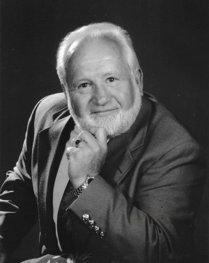 A black and white photo of Ronald Wrightman, Co-founder of True North Log & Timber Homes. Ron makes eye contact with the camera and has a slight smile. 