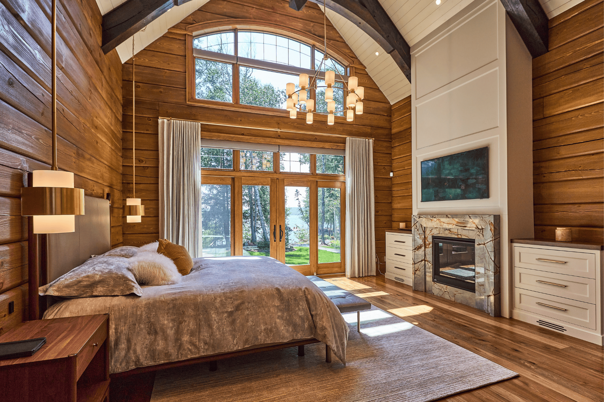 This is the master bedroom of True North Log & Timber Homes’s award-winning Colantonio Residence. This home invites in the warmth of sunlight and the stunning lake-side vista with its floor-to-ceiling windows.